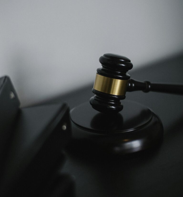 Black wooden gavel with golden strip on table near stack of folders in courthouse