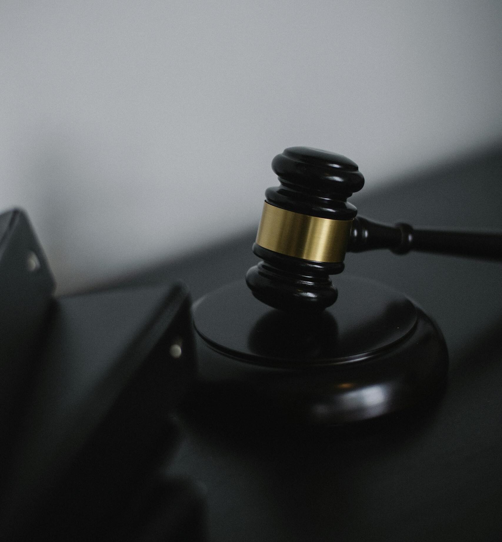 Black wooden gavel with golden strip on table near stack of folders in courthouse