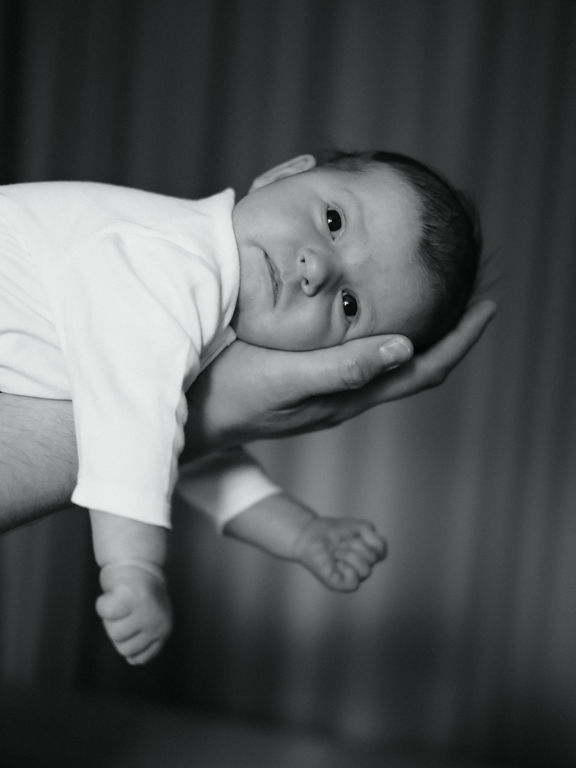 Emotional black and white photo of a newborn baby supported by a loving hand.